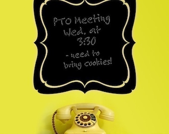 May include: A black chalkboard with a decorative border displays the text "PTO Meeting Wed. at 3:30 - need to bring cookies!" A vintage cream-colored rotary dial telephone sits below the chalkboard on a white shelf against a yellow wall.
