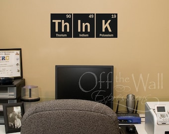 May include: A black and white wall decal with the periodic table elements Thorium (Th), Indium (In), and Potassium (K) arranged to spell the word "Think". The decal is on a beige wall in an office setting.