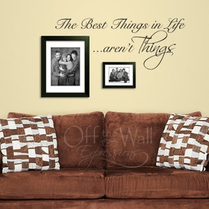 May include: A brown couch with two pillows featuring a black and white checkered pattern. The wall behind the couch has a black vinyl decal with the text "The Best Things in Life...aren't Things".