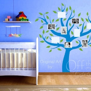 May include: A blue and green tree wall decal with blank photo frames, perfect for a nursery or child's room. The decal is on a light blue wall with a white crib in the foreground. The text "Original Art by: Off the Wall Expressions" is visible at the bottom of the image.