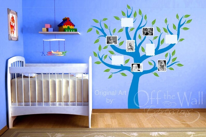May include: A blue and green tree wall decal with blank photo frames, perfect for a nursery or child's room. The decal is on a light blue wall with a white crib in the foreground. The text "Original Art by: Off the Wall Expressions" is visible at the bottom of the image.