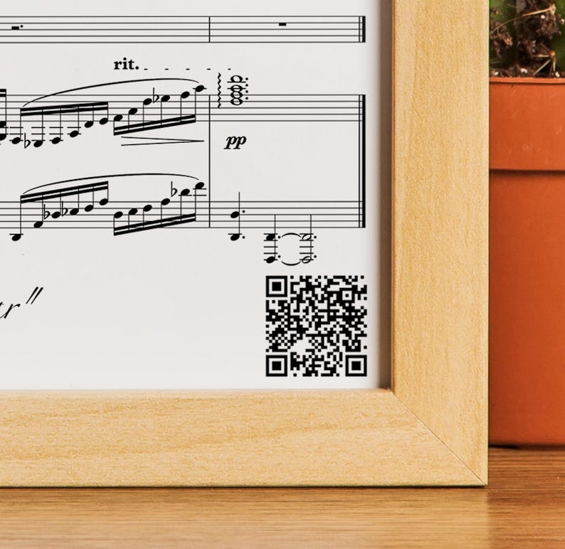 May include: A framed sheet of music with a QR code in the bottom right corner. The music is written in black ink on white paper and includes musical notes, a musical key signature, and the word "rit."