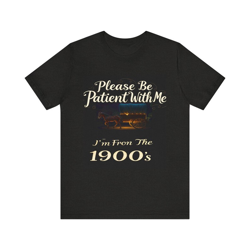 May include: Dark heather gray t-shirt featuring a vintage-style design. The text reads, 'Please Be Patient With Me I'm From The 1900's.'  An image of a horse-drawn wagon is displayed above the text. The design is in cream-colored lettering against a dark background.