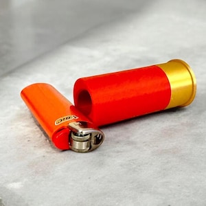 May include: A red and gold lighter with a silver mechanism. The lighter is on a gray surface.