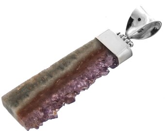 Puede incluir: Un colgante de plata con un cristal de amatista en bruto con una textura natural y rugosa. El cristal es de color púrpura claro y tiene una banda marrón y gris que lo atraviesa. El colgante está unido a una argolla de plata.