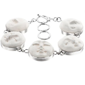 Op de afbeelding: Een zilveren armband met vijf ronde witte keramische bedels, elk met een andere gegraveerde gezichtsuitdrukking.