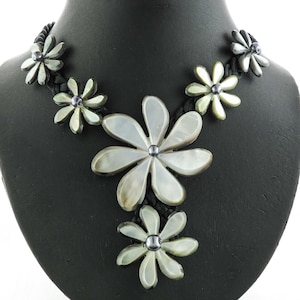 May include: A black braided necklace with white mother of pearl flower pendants. The flowers have a silver center and are arranged in a cascading pattern.