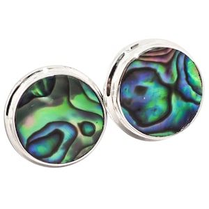 May include: Two round cufflinks with iridescent abalone shell inlays. The shell displays a mix of green, blue, and purple hues, set in a polished silver metal frame. The cufflinks are designed for formal wear.