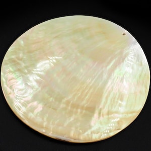 May include: A large, round, white mother of pearl shell with a hole drilled in the top. The shell has a smooth, iridescent surface with a subtle pattern of lines.