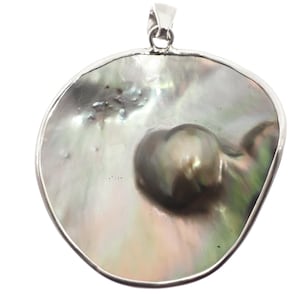 Op de afbeelding: Een grote, iriserende parel hanger met een zilverkleurige rand. De parel heeft een glanzend, wervelend patroon van grijs, groen en wit. De hanger heeft een lus aan de bovenkant voor een ketting.