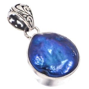 Può includere: Un ciondolo blu iridescente a forma di goccia, con montatura color argento. Il ciondolo ha una superficie strutturata e un'ansa decorativa con un design ornato. Il gioiello è posto su sfondo bianco.