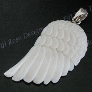May include: White carved bone angel wing pendant with a silver bail. The wing is detailed with a feathered design.
