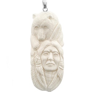 May include: A white carved pendant featuring a Native American chief with a bear on his head. The pendant is made of bone and has a silver bail.