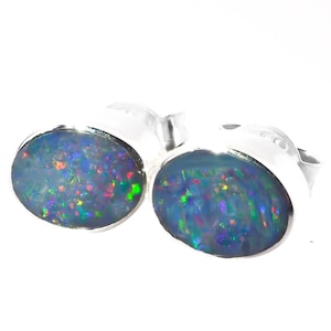 May include: A pair of silver stud earrings with oval-shaped blue opals that have iridescent rainbow flashes.