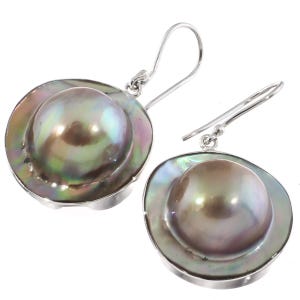 Puede incluir: Un par de pendientes de perlas mabe con grandes perlas grises iridiscentes en forma de cúpula montadas en plata. Cada perla tiene un centro liso y redondeado rodeado por un borde plano y brillante con sutiles tonos verdes y púrpuras, con ganchos.