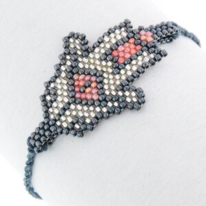May include: A black and silver beaded bracelet with a red and white beaded design in the shape of a fish.
