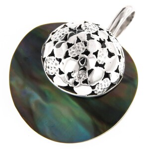 Könnte beinhalten: Ein silberner Anhänger mit einem filigranen Blumendesign, auf einer dunkelgrünen Abalone-Muschel.