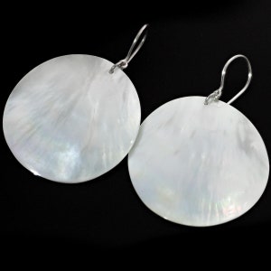 May include: A pair of white mother-of-pearl earrings with silver hooks. The earrings are round and have a smooth, iridescent finish.