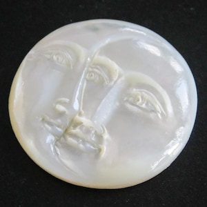 Op de afbeelding: Een witte parelmoer cameo met een gegraveerd beeld van twee gezichten, één aan elke kant van de maan.