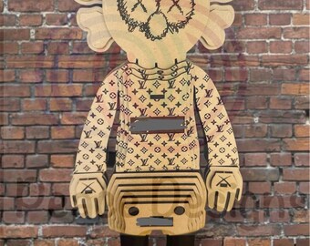 May include: A wooden art figure with a unique design stands against a brick wall. The figure has a head with crossed-out eyes and a patterned shirt. The figure's body is tan, with black accents and yellow shoes.