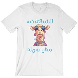 May include: White t-shirt featuring a cartoon camel wearing sunglasses and a colourful necklace. The text "مش سولة" and "الشباكة دي" is printed on the shirt.