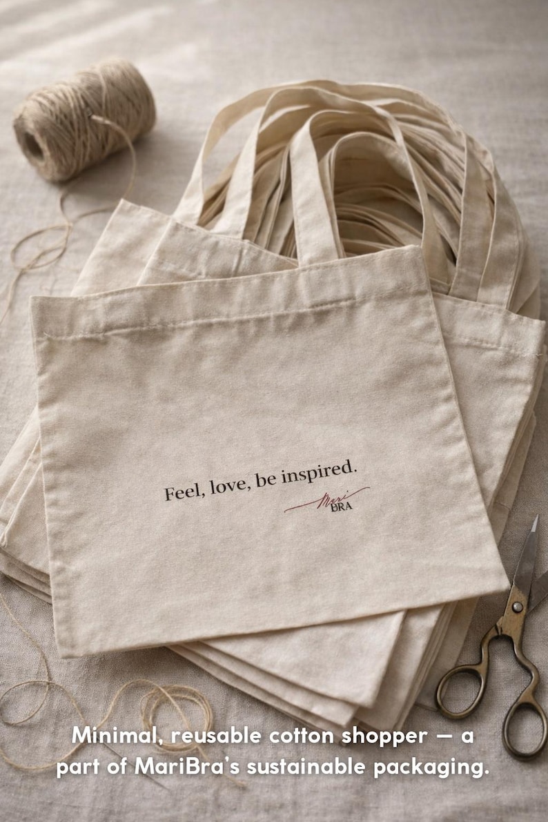 Puede incluir: Un mont&oacute;n de bolsas de mano de algod&oacute;n beige con asas, cada una impresa con las palabras "Feel, love, be inspired." y una firma. Tambi&eacute;n se ven un carrete de hilo y unas tijeras. Las bolsas forman parte de una l&iacute;nea de embalaje sostenible.