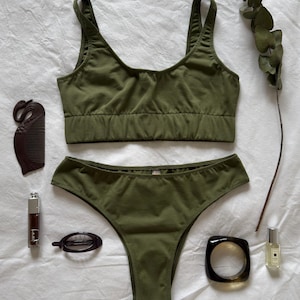 May include: Olive green lingerie set with a matching bralette and high-cut briefs. Accessories include a brown comb, lipstick, hair clip, bracelet, and perfume bottle. A sprig of eucalyptus adds a natural touch.