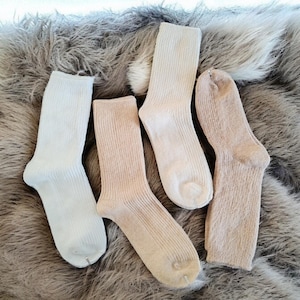 May include: Four pairs of socks, two white and two beige, laid out on a fluffy brown surface.