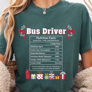 Puede incluir: Una camiseta verde oscuro con la frase "Bus Driver" en blanco, adornada con gráficos navideños. Debajo, una etiqueta de "Nutrition Facts" enumera valores humorísticos relacionados con la Navidad. Una prenda festiva y divertida para las vacaciones.