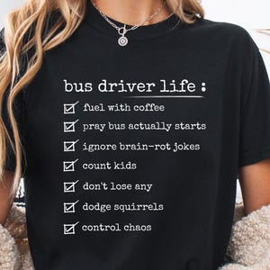 Puede incluir: Camiseta negra con texto blanco que dice "bus driver life:" (vida de conductor de autobús) y una lista de tareas, incluyendo tomar café, contar niños y esquivar ardillas.