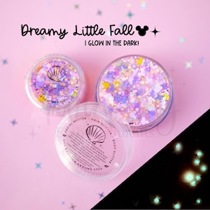 May include: Two clear circular containers filled with iridescent, multi-colored glitter in various shapes, including small mouse silhouettes. The lids feature a seashell icon and text reading Dreamy Little Fall I GLOW IN THE DARK.