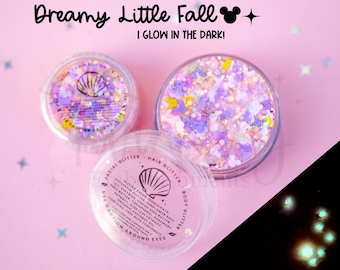 May include: Two clear circular containers filled with iridescent, multi-colored glitter in various shapes, including small mouse silhouettes. The lids feature a seashell icon and text reading Dreamy Little Fall I GLOW IN THE DARK.