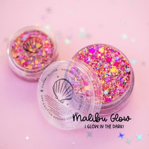 Könnte beinhalten: Drei transparente Tiegel mit Gesichtsgelitter mit einem Muschel-Logo, gefüllt mit bunten Glitzer in Rosa-, Lila- und Gelbtönen. Der Text "Malibu Glow" und "I GLOW IN THE DARK!" sind auf einem rosa Hintergrund abgebildet.