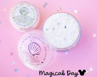 May include: Two clear circular containers filled with iridescent white body glitter. Each lid features a black seashell icon, the text "FACIAL GLITTER - HAIR GLITTER - BODY GLITTER", and "USE CAUTION AROUND EYES". The text "Magical Day" appears below.