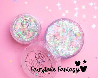 May include: Two clear circular jars filled with iridescent, multi-colored glitter creme. The lids feature a seashell icon, the text "FACIAL GLITTER HAIR GLITTER BODY GLITTER," and ingredient lists. The text "Fairytale Fantasy" appears nearby.