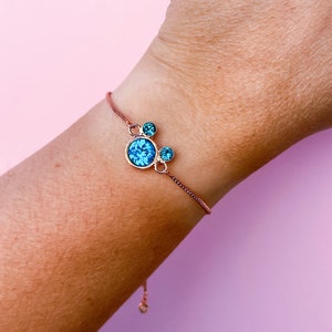 May include: A rose gold bracelet with a blue crystal charm in the shape of a Mickey Mouse head.