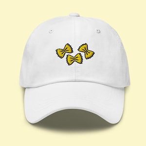 Könnte beinhalten: Weiße Baseballkappe mit einem gestickten Design aus drei gelben Farfalle-Nudeln. Die Kappe hat einen gebogenen Schirm und einen verstellbaren Riemen. Die Nudelformen sind schwarz umrandet.