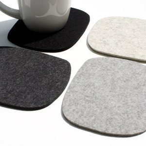 May include: Four felt coasters, two gray and two black, in a square shape with rounded corners. The coasters are made of a soft, textured material.