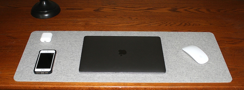 May include: A gray felt desk mat with a laptop computer, a smartphone, a pair of wireless earbuds, and a wireless mouse.