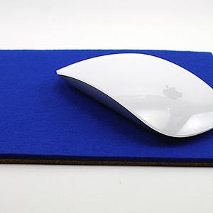 Peut inclure: Un tapis de souris en feutre bleu avec une souris sans fil blanche sur le dessus. La souris a un logo Apple argenté sur le dessus.