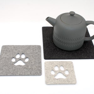 May include: Two gray felt coasters with paw print cutouts. A gray teapot sits on a black felt coaster.