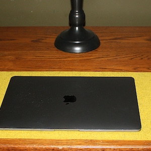 May include: A yellow felt desk mat with a black laptop computer, a white wireless mouse, and a white smartphone on a wooden desk.
