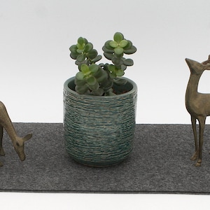 May include: Two bronze deer figurines on a gray felt mat with a potted succulent plant in a blue and green ceramic pot.