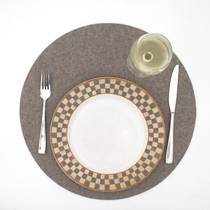 Puede incluir: Un mantel individual de fieltro gris con un plato blanco con un patr&oacute;n de cuadros marrones y negros. Un vaso de vino blanco y un tenedor y cuchillo plateados est&aacute;n en el mantel individual.