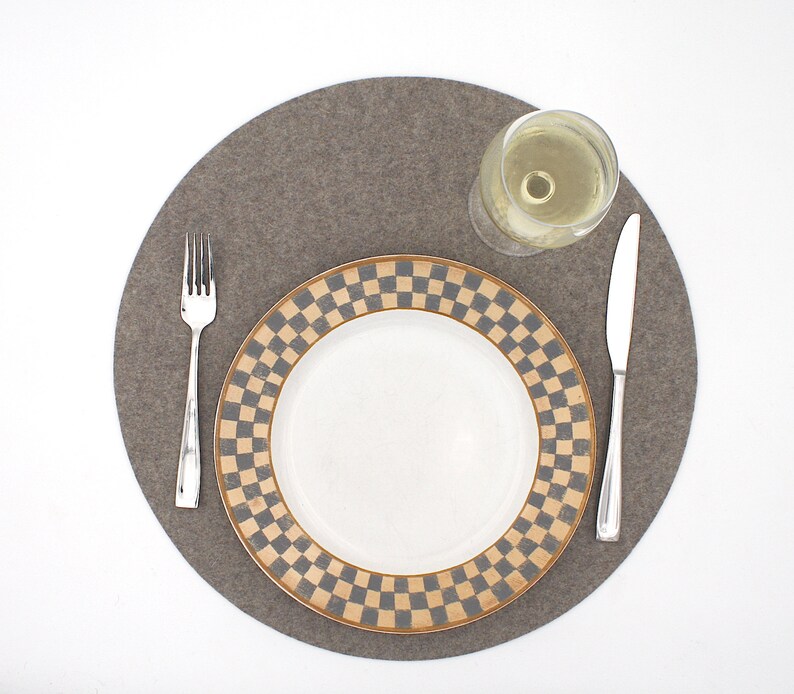 Puede incluir: Un mantel individual de fieltro gris con un plato blanco con un patr&oacute;n de cuadros marrones y negros. Un vaso de vino blanco y un tenedor y cuchillo plateados est&aacute;n en el mantel individual.