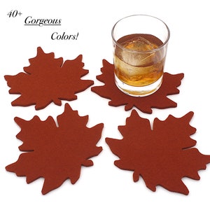 May include: Four rust-colored felt coasters shaped like maple leaves. One coaster supports a clear glass containing an amber liquid and a single ice cube. The text 40+ Gorgeous Colors! appears in the upper left corner of the image.