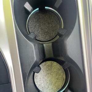 May include: Two black cup holders with gray felt liners. The cup holders are in a car.