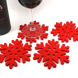 May include: Four red felt snowflake coasters with a wine glass sitting on one of them. The wine glass is filled with red wine.