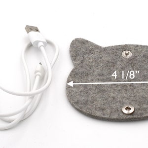 May include: A grey felt cat-shaped cord organiser with two silver snaps and a white USB charging cable. The organiser measures 10.5 cm wide.