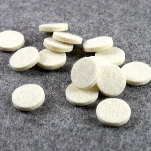 May include: A pile of white felt circles, likely furniture pads, on a gray felt surface.
